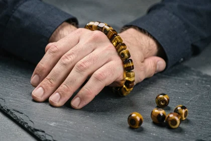 Bracelet homme en œil de tigre sur poignet masculin, gros plan sur les perles dorées aux reflets chatoyants posé sur ardoise sombre