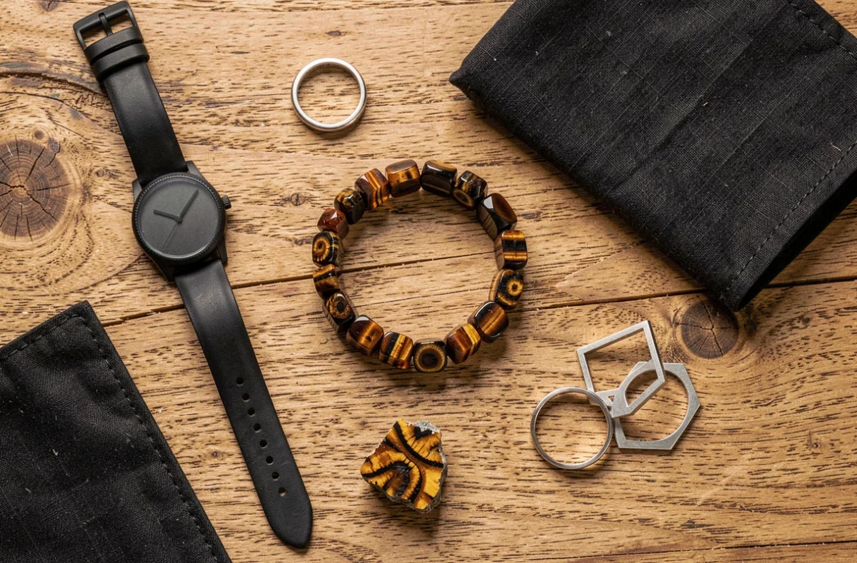 Flat lay d'accessoires homme avec bracelet en œil de tigre, montre cuir et pierre brute sur bois naturel vieilli