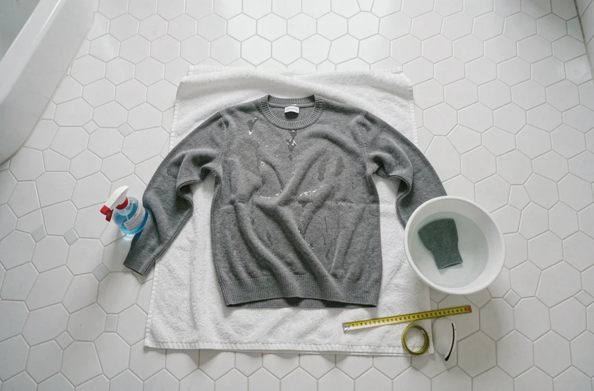 Pull en laine rétréci étalé sur une serviette avec des outils pour le remettre à taille originale dans une salle de bain
